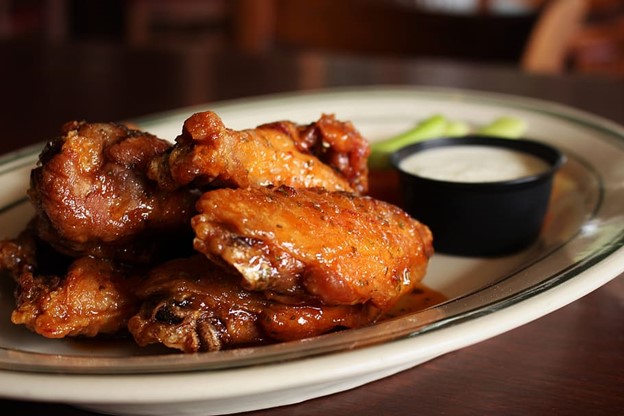 Crispy chicken wings on glass platter next to a small bowl of sauce